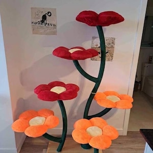 May include: A whimsical cat tree designed as a flower arrangement. It features multiple plush flower platforms in red and orange, with green stems and a light wood base. The cat tree is a unique piece of pet furniture.