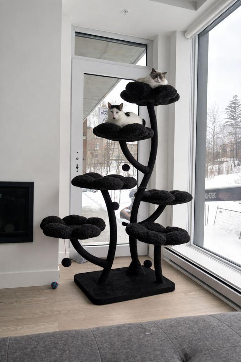 May include: A black cat tree with flower-shaped platforms. Two cats are resting on the top platforms. The cat tree is made of a soft, plush material and has a sturdy base. The cat tree is placed near a window in a home.