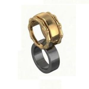 May include: Two rings, one gold-colored and one dark gray, are stacked. The top ring has a bamboo-like design, while the bottom ring is a simple band. The rings are likely made of metal and are displayed against a white background.
