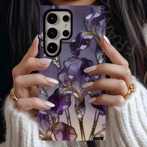 May include: A rectangular smartphone case featuring a vibrant stained-glass style illustration of purple iris flowers with gold accents. The design includes multiple camera lenses in the upper left corner and a smooth, glossy finish throughout.