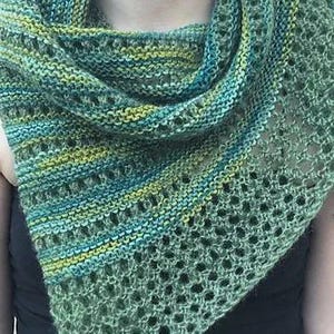 Peut inclure: Un châle tricoté à la main dans des tons de vert, de sarcelle et de jaune. Le châle présente un motif texturé avec des sections ajourées. La laine semble douce et le châle est drapé autour des épaules.