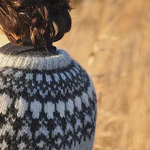 May include: A close-up of a gray and white patterned sweater. The sweater has a crew neck and a geometric design in black and white. The person's brown hair is visible.