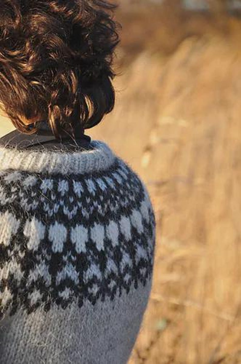 May include: A close-up of a gray and white patterned sweater. The sweater has a crew neck and a geometric design in black and white. The person's brown hair is visible.