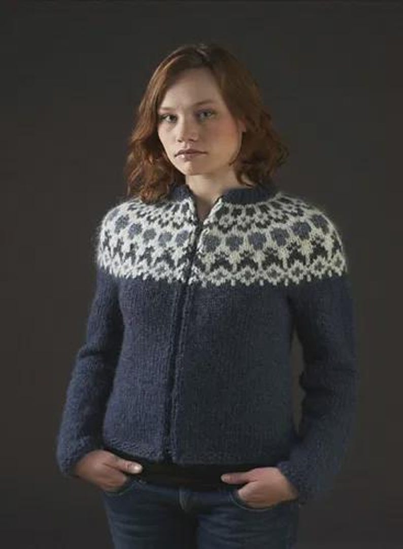 May include: A navy blue zip-up sweater with a patterned yoke in white, gray, and black. The sweater has long sleeves and is made of a textured knit fabric. The model is wearing blue jeans.