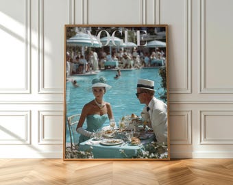 May include: A framed Vogue magazine cover featuring a woman in a turquoise dress and hat, seated at a table with a man in a white suit. The background shows a pool and people, with the Vogue logo at the top.