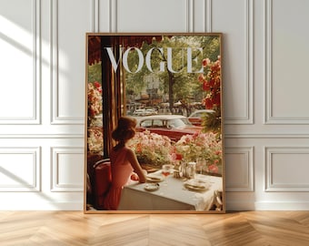 May include: A framed Vogue magazine cover print featuring a woman in a pink dress seated at a table, with a view of a street scene. The Vogue logo is at the top. The print has a vintage, romantic aesthetic with a warm color palette.