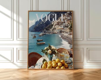 Op de afbeelding: Een ingelijste kunstdruk met een tijdschriftomslag met de titel VOGUE. De afbeelding toont een kustlandschap met een turquoise zee, kleine boten en gebouwen op een heuvel. Op de voorgrond staat een ronde tafel met een schaal gele citroenen.
