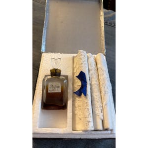 May include: An antique perfume set in a silver box. The set includes a small, square perfume bottle with a decorative stopper, and several rolled white lace handkerchiefs tied with a blue ribbon. The perfume bottle has a label with elegant script.