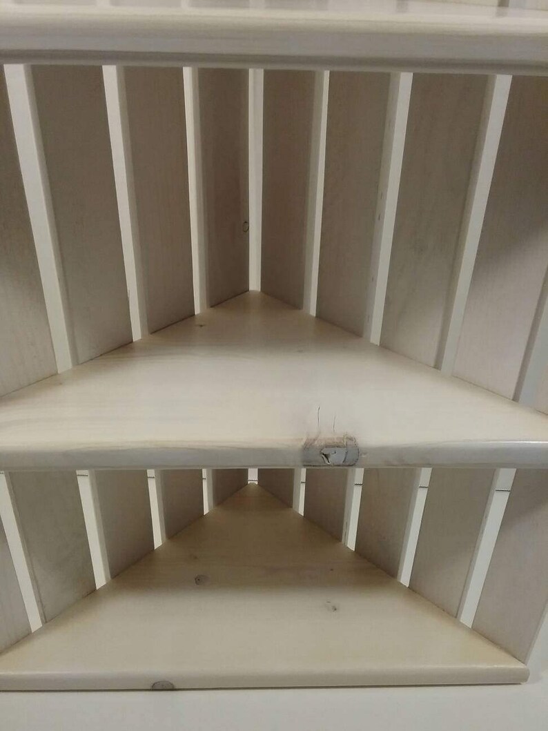 May include: White corner shelf unit with three shelves. The shelves are made of wood and have a slatted design.