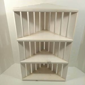 May include: White corner shelf unit with three shelves. The shelves are made of wood and have a simple design.