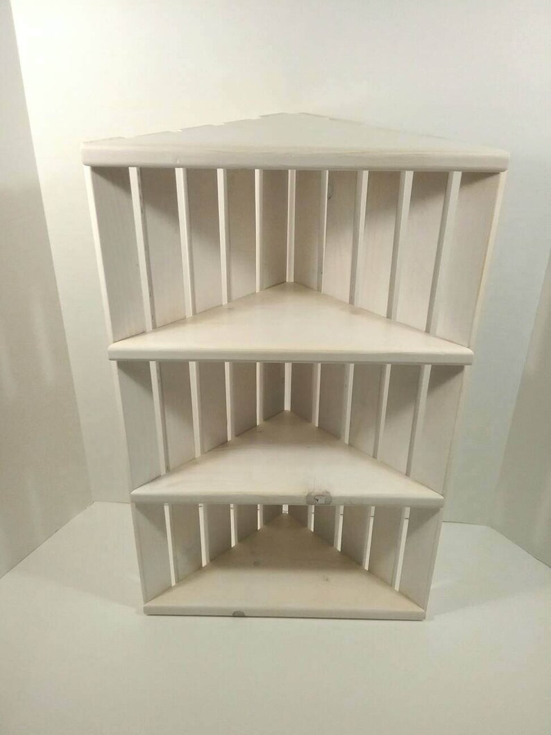 May include: White corner shelf unit with three shelves. The shelves are made of wood and have a simple design.
