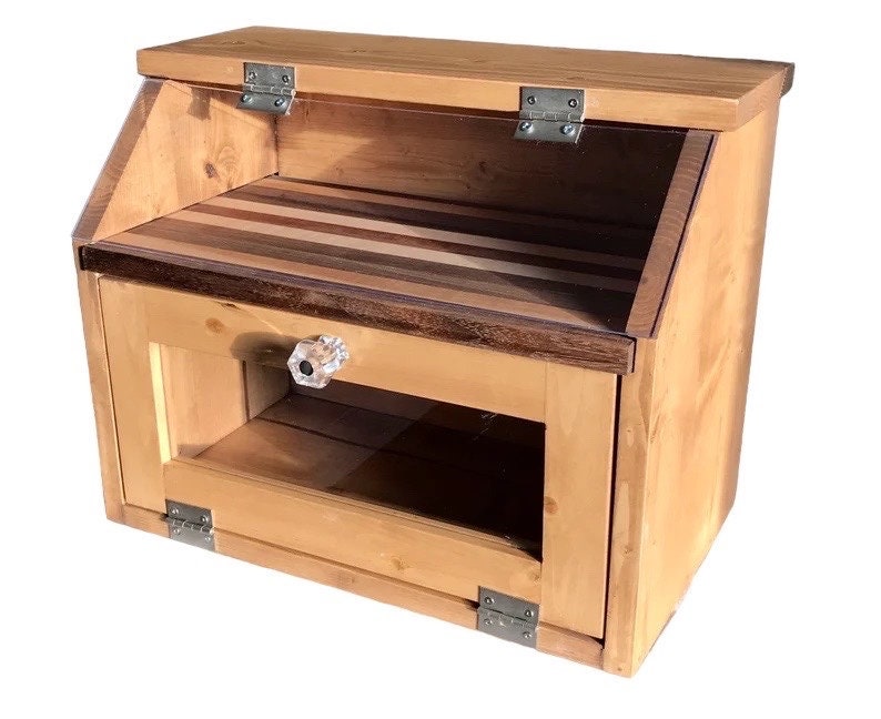 Handcrafted wooden bread box with front compartment that has clear polycarbonate Lexan, and a multi-wood bread board.  The front has clear knob handle and silver hinges.  Color shown is Monarch.