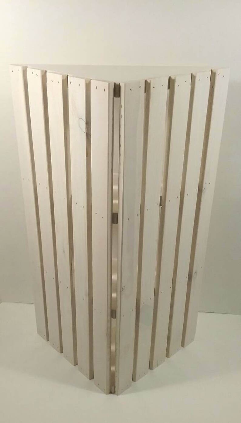 May include: White wooden corner shelf with a slatted design. The shelf is made of unfinished wood and has a rustic look.