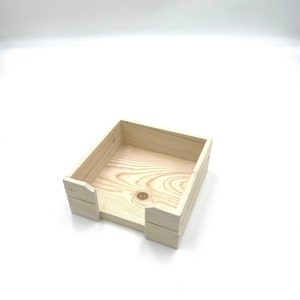 May include: A natural wood square tissue box holder with a simple design. The holder is made of unfinished wood and has a slot for tissues to be pulled out.