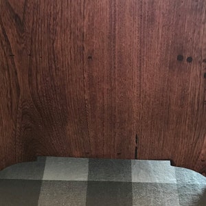 May include: A rectangular wooden furniture piece with a rich, dark brown finish and a prominent vertical wood grain pattern. The base features two arched cutouts at the bottom, creating four distinct feet that support the solid structure.