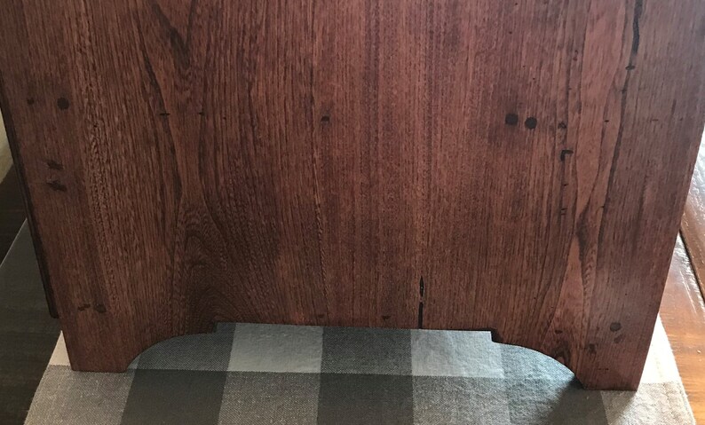 May include: A rectangular wooden furniture piece with a rich, dark brown finish and a prominent vertical wood grain pattern. The base features two arched cutouts at the bottom, creating four distinct feet that support the solid structure.