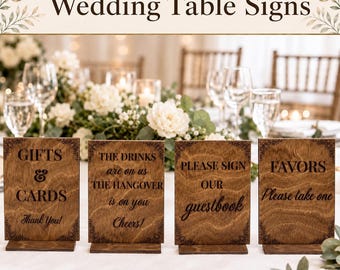 May include: Four rectangular wooden table signs with dark brown wood grain and black engraved text. The signs feature decorative corner patterns and include the phrases: Gifts & Cards, The drinks are on us, Please sign our guestbook, and Favors.
