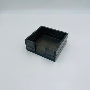 May include: A black wooden box with a square shape and a small opening on one side. The box is designed to hold and dispense tissues.