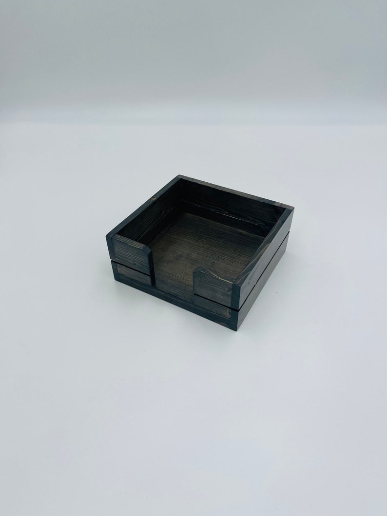 May include: A black wooden box with a square shape and a small opening on one side. The box is designed to hold and dispense tissues.