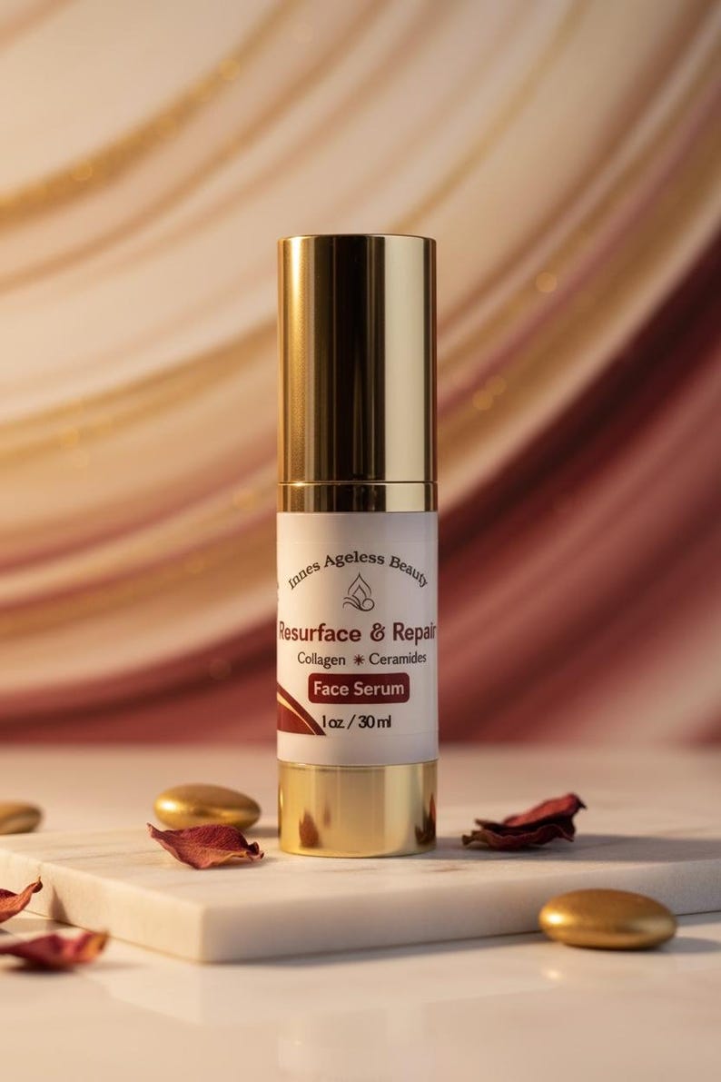 May include: A gold and white face serum bottle with the text "Resurface & Repair" and "Face Serum." The bottle is on a white marble surface with gold accents and dried rose petals.
