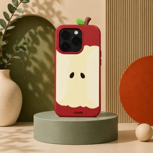 May include: A red smartphone case featuring a graphic of a partially eaten apple core with a small green leaf and brown stem at the top. The case has a cutout for a triple camera system and the word Apple printed in small black letters at the bottom.