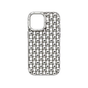 Puede incluir: Una funda para teléfono de color plateado con una estructura de rejilla compuesta por numerosas esferas metálicas pequeñas y reflectantes. El diseño incluye un recorte rectangular en la esquina superior izquierda para la cámara.