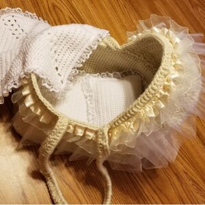 May include: A crocheted heart-shaped basket with a white crocheted blanket inside. The basket is decorated with white and gold lace and ribbons.