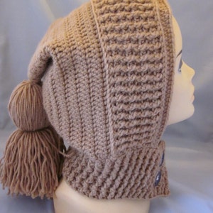 Può includere: Un cappello a uncinetto marrone con un lungo fiocco pendente. Il cappello ha un'ampia tesa e una corona a punta. Il cappello è indossato sulla testa di un manichino.