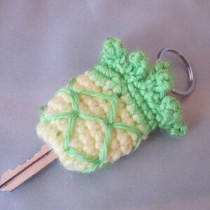 May include: A crocheted pineapple keychain with a green top and yellow body attached to a silver key ring.