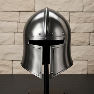 May include: A silver-colored medieval helmet with a visor and riveted details, displayed on a black stand. The helmet has a smooth, reflective surface and is designed with a rounded top and a rectangular opening for the eyes.