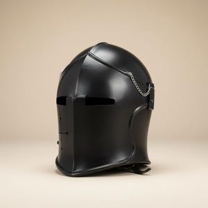 Pu&ograve; includere: Un elmo da cavaliere nero con visiera e dettagli a catena. L'elmo &egrave; realizzato in un materiale liscio e scuro e presenta fessure per gli occhi e un sottogola. Il design ricorda l'armatura medievale.