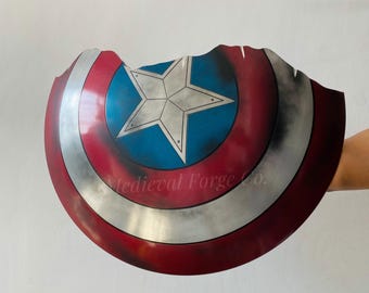 May include: A distressed Captain America shield, featuring a blue center with a white star, surrounded by red and silver concentric rings. The shield has a battle-worn appearance with a jagged edge. The text "Medieval Forge Co." is visible on the shield.