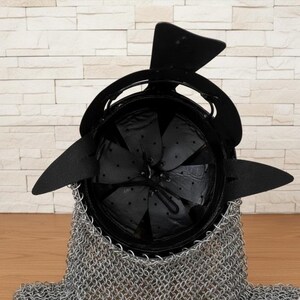 以下が含まれることがあります： 黒い金属製のヘルメットとチェーンメイルのネックガード。ヘルメットは丸みを帯びた形状で、黒い尖った延長部と中央のフィンが付いています。内側は黒い布で裏打ちされています。チェーンメイルはシルバーです。