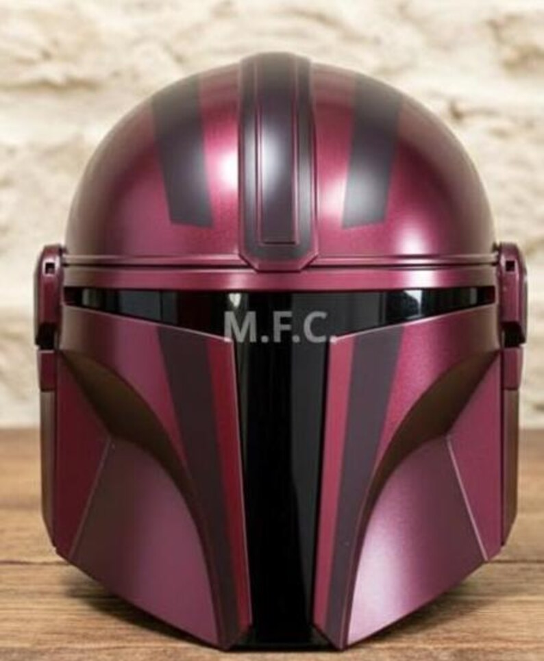 Pu&ograve; includere: Un casco bordeaux e nero con la scritta "M.F.C." &egrave; in mostra. Il casco ha una parte superiore arrotondata con strisce verticali e elementi angolari intorno al viso. La visiera &egrave; nera e il design generale suggerisce un tema futuristico o fantascientifico.