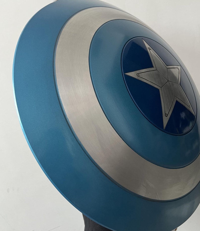 May include: A blue and silver shield with a central star design. The shield has a circular shape with concentric rings of blue and silver. The star is silver and has a five-pointed design. The shield is a prop.