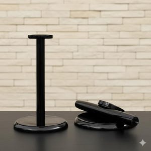 May include: Black, glossy, modern hat stand with a round base and a cylindrical pole, next to a black hat brim and a cylindrical hat body. The stand is on a black surface with a light-colored brick wall in the background.