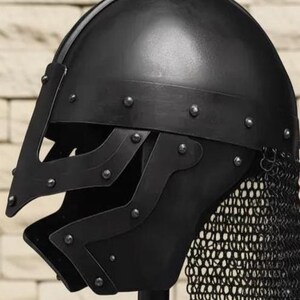 May include: A black medieval helmet with a riveted construction and a chainmail neck guard. The helmet features a visor with cutouts and is designed for protection. The dark color and detailed craftsmanship suggest historical reenactment or costume use.