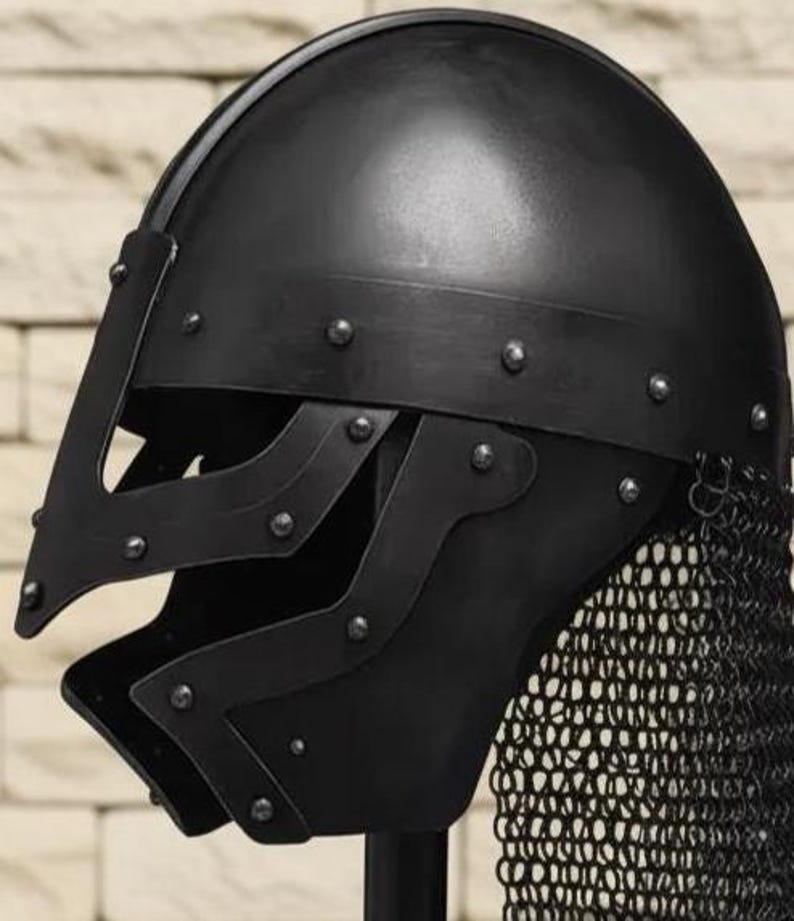 May include: A black medieval helmet with a riveted construction and a chainmail neck guard. The helmet features a visor with cutouts and is designed for protection. The dark color and detailed craftsmanship suggest historical reenactment or costume use.