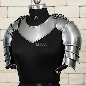 May include: Silver-colored metal armor set, including a chest plate and shoulder guards, displayed on a black mannequin. The armor features articulated shoulder plates and is secured with leather straps. The text "M.F.C." is visible on the chest plate.