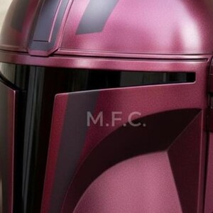 Pu&ograve; includere: Primo piano di un casco bordeaux con dettagli neri. Il casco ha una finitura metallica liscia e le lettere "M.F.C." sono visibili. Il design suggerisce un tema futuristico o di fantascienza.