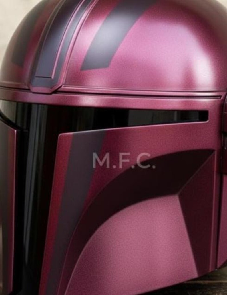Pu&ograve; includere: Primo piano di un casco bordeaux con dettagli neri. Il casco ha una finitura metallica liscia e le lettere "M.F.C." sono visibili. Il design suggerisce un tema futuristico o di fantascienza.