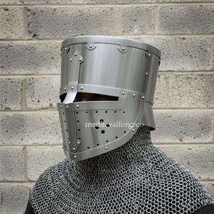May include: A silver-colored, riveted medieval helmet with a visor and numerous small ventilation holes. The helmet is worn over a chainmail coif. The text "medievalforgeco" is visible on the helmet.