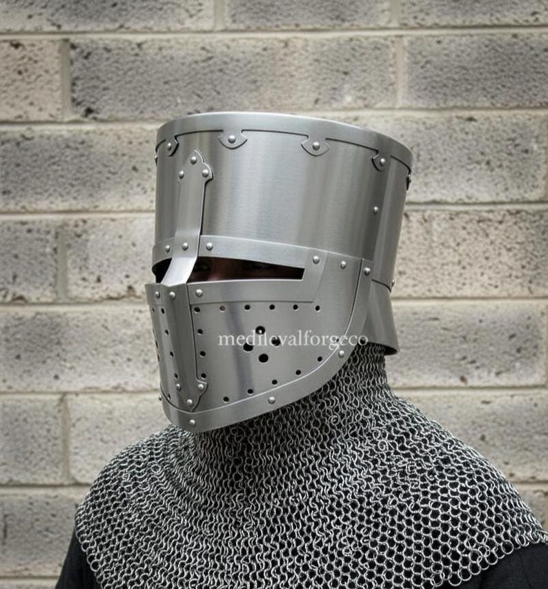 May include: A silver-colored, riveted medieval helmet with a visor and numerous small ventilation holes. The helmet is worn over a chainmail coif. The text "medievalforgeco" is visible on the helmet.