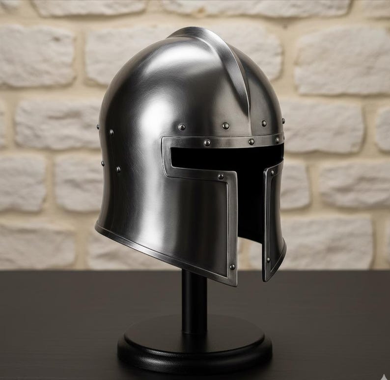 May include: A silver-colored medieval helmet with a visor, rivets, and a central ridge. The helmet is displayed on a black stand with a round base, set against a brick wall background.
