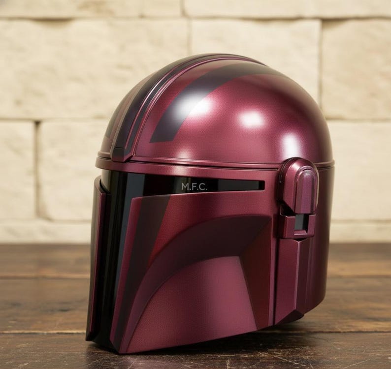 Pu&ograve; includere: Un casco bordeaux con dettagli neri e la scritta "M.F.C." sul davanti. Il casco ha una finitura lucida e un design che ricorda un casco Mandaloriano.