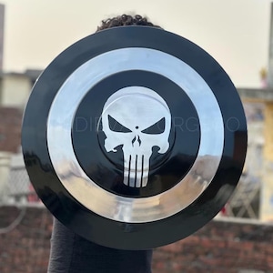 Op de afbeelding: Een cirkelvormig schild met een gepolijste zilveren afwerking, een opvallende zwarte rand en een zilveren schedel-embleem in het midden. Het ontwerp bevat concentrische ringen en een gestileerde schedelafbeelding in het midden.