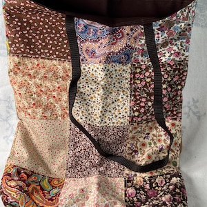 Peut inclure: Un sac fourre-tout patchwork avec divers motifs floraux et cachemire dans des tons de marron, beige et bordeaux. Le sac a un intérieur marron foncé et des sangles noires. Le sac est en tissu.