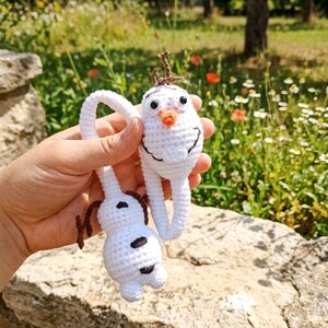 Puede incluir: Dos adornos de mu&ntilde;eco de nieve de ganchillo blanco con ojos negros, nariz de zanahoria y pelo casta&ntilde;o. Un mu&ntilde;eco de nieve est&aacute; en posici&oacute;n vertical y el otro al rev&eacute;s. Los mu&ntilde;ecos de nieve est&aacute;n sostenidos por un lazo de ganchillo blanco.