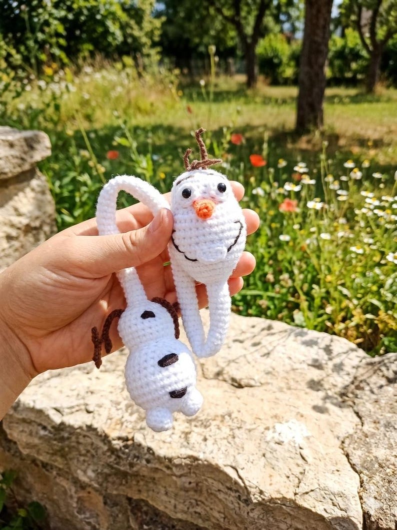 Puede incluir: Dos adornos de mu&ntilde;eco de nieve de ganchillo blanco con ojos negros, nariz de zanahoria y pelo casta&ntilde;o. Un mu&ntilde;eco de nieve est&aacute; en posici&oacute;n vertical y el otro al rev&eacute;s. Los mu&ntilde;ecos de nieve est&aacute;n sostenidos por un lazo de ganchillo blanco.