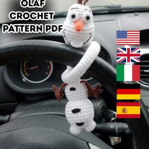 Puede incluir: Un accesorio de coche Olaf de ganchillo blanco con nariz de zanahoria y pelo casta&ntilde;o. El accesorio cuelga del volante de un coche. El texto "OLAF CROCHET PATTERN PDF" es visible.